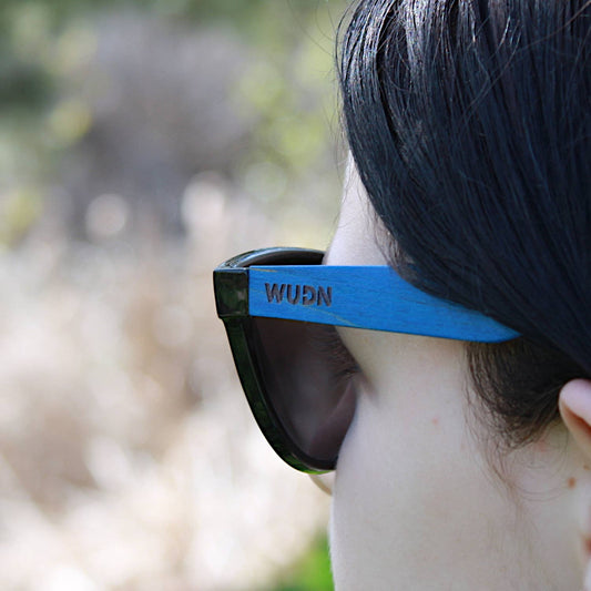 escalator blue hybrid recycled sunglasses with a blue frame and 'WUDN' logo, outdoors.
