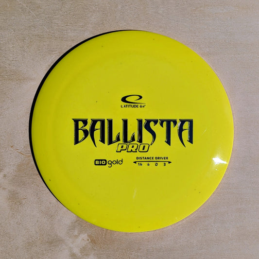 Yellow disc golf disc with 'Ballista Pro' branding on a beige surface