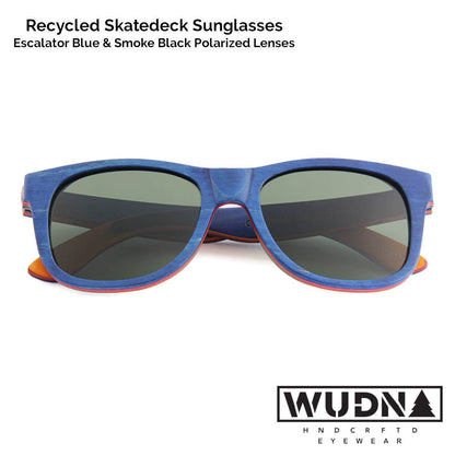 Escalator blue Recycled skatedeck sunglasses with blue frame and dark lenses on a white background, featuring WUDN logo.