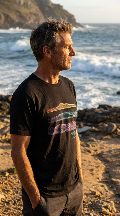 black Man standing on a rocky beach with ocean waves and cliffs in the background