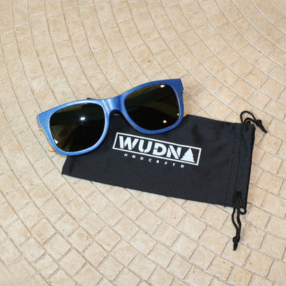 Escalator blue Recycled sunglasses on a black drawstring bag with 'WUDN' branding on a tiled floor.