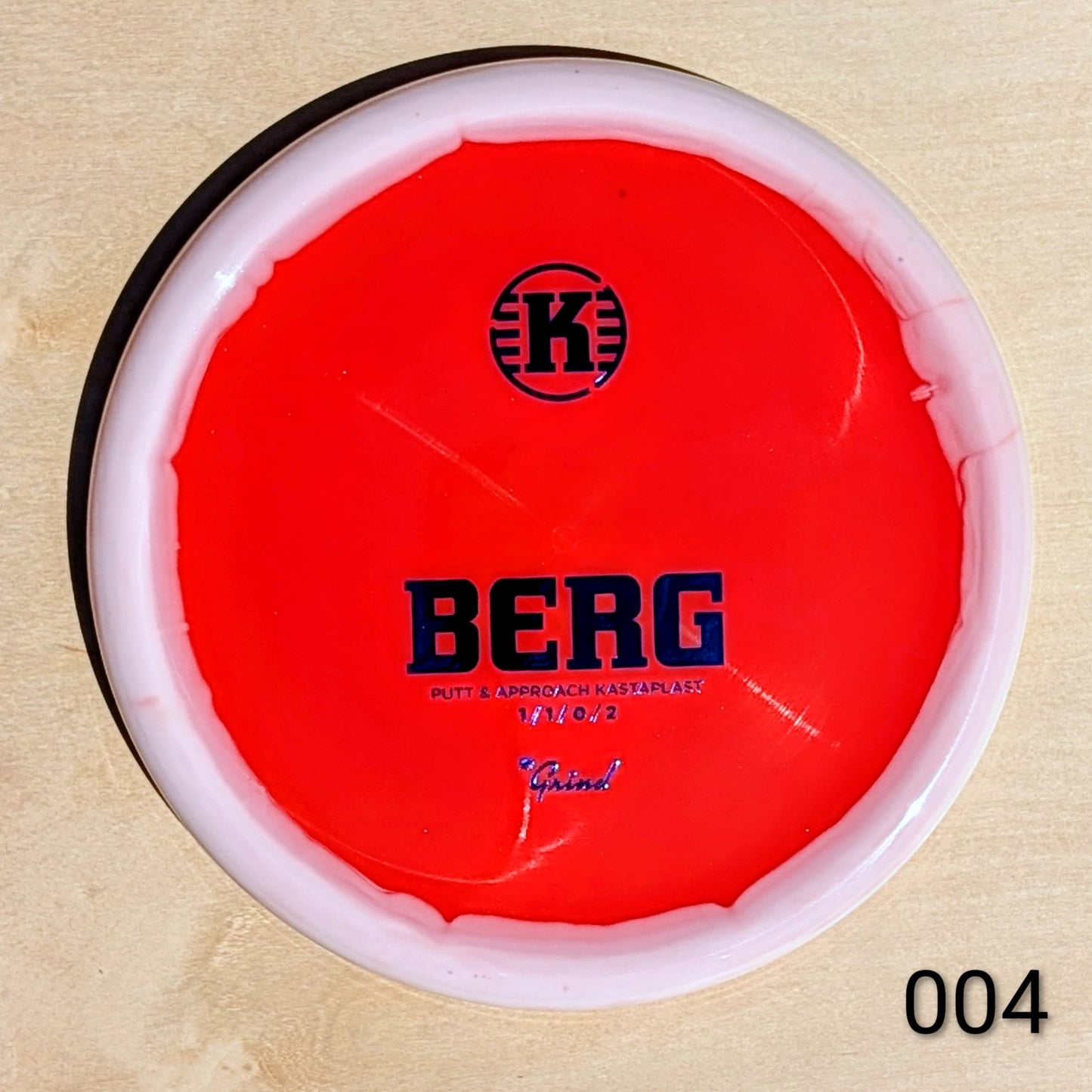Red disc golf putter with 'K' logo and 'BERG' text on a beige background