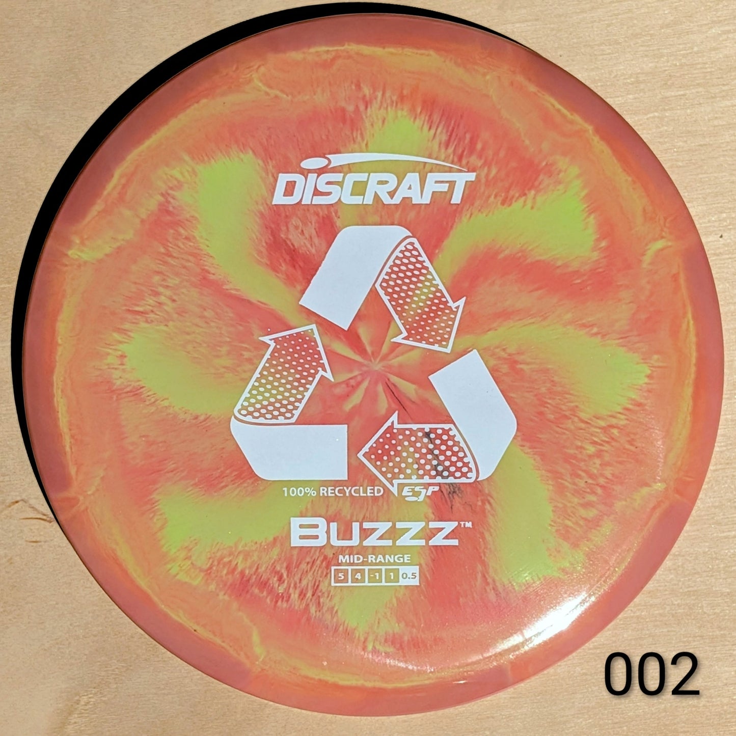Discraft Buzzz disc golf disc with a swirling red and green design on a beige background