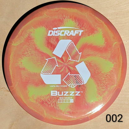 Discraft Buzzz disc golf disc with a swirling red and green design on a beige background
