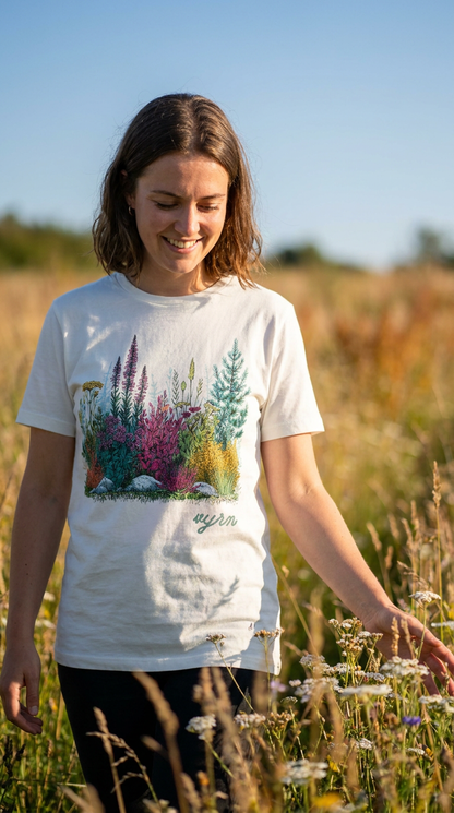 white Woman wearing a white t-shirt with a nature-themed design in a field