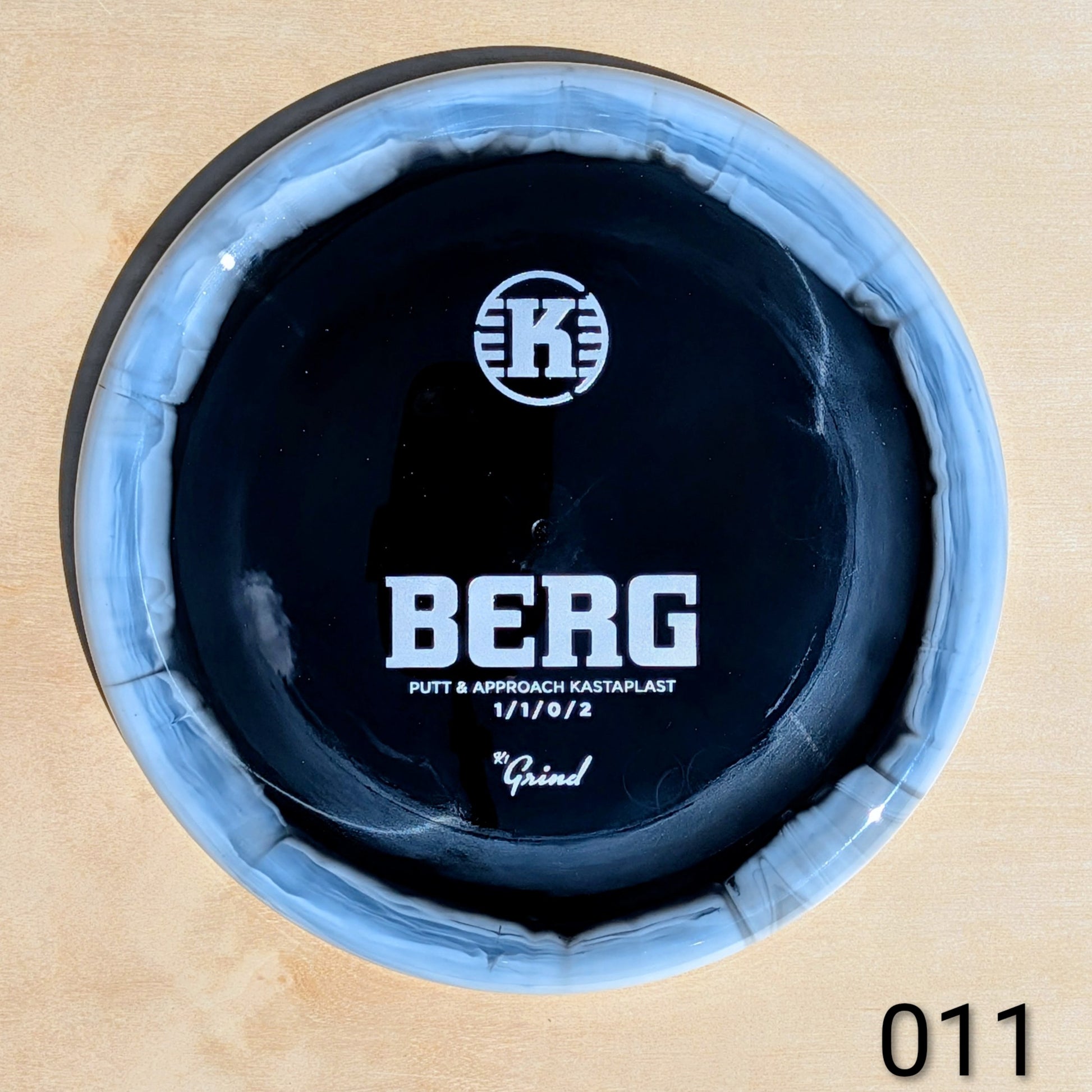 Close-up of a putter head with 'K' logo and 'BERG' branding on a wooden background.
