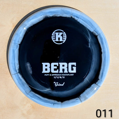 Close-up of a putter head with 'K' logo and 'BERG' branding on a wooden background.