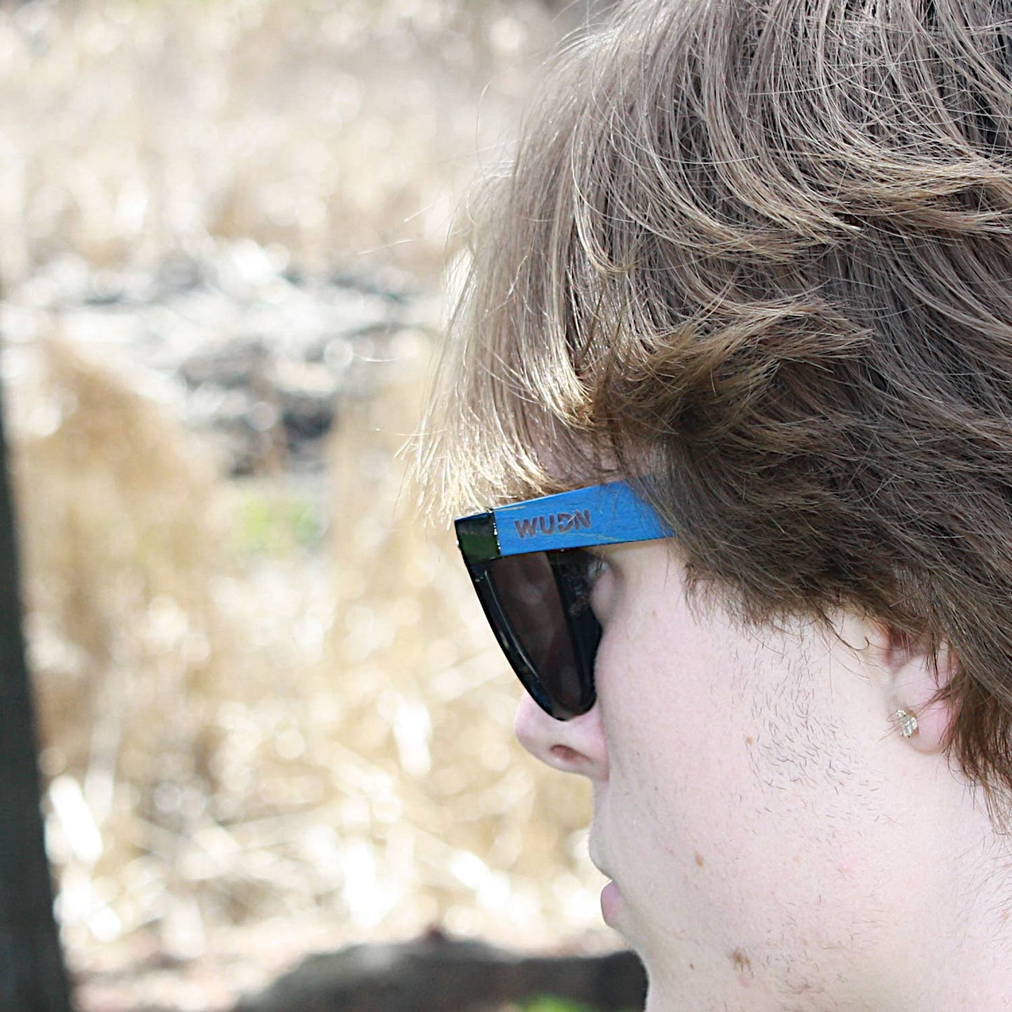 escalator blue hybrid recycled sunglasses with a blurred natural background