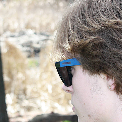 escalator blue hybrid recycled sunglasses with a blurred natural background