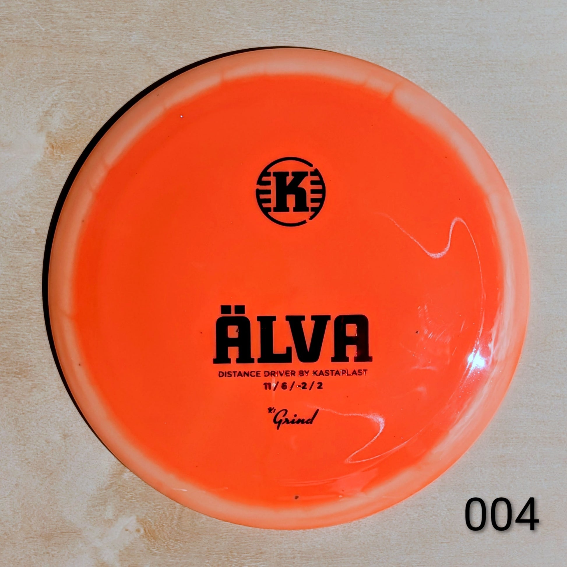 Orange disc golf disc with 'K' logo and text on a beige background