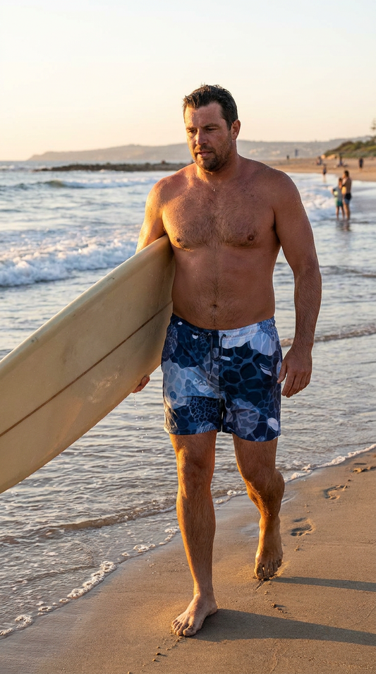 Rockpool Channel Man walking on a beach holding a surfboard with a sunset in the background